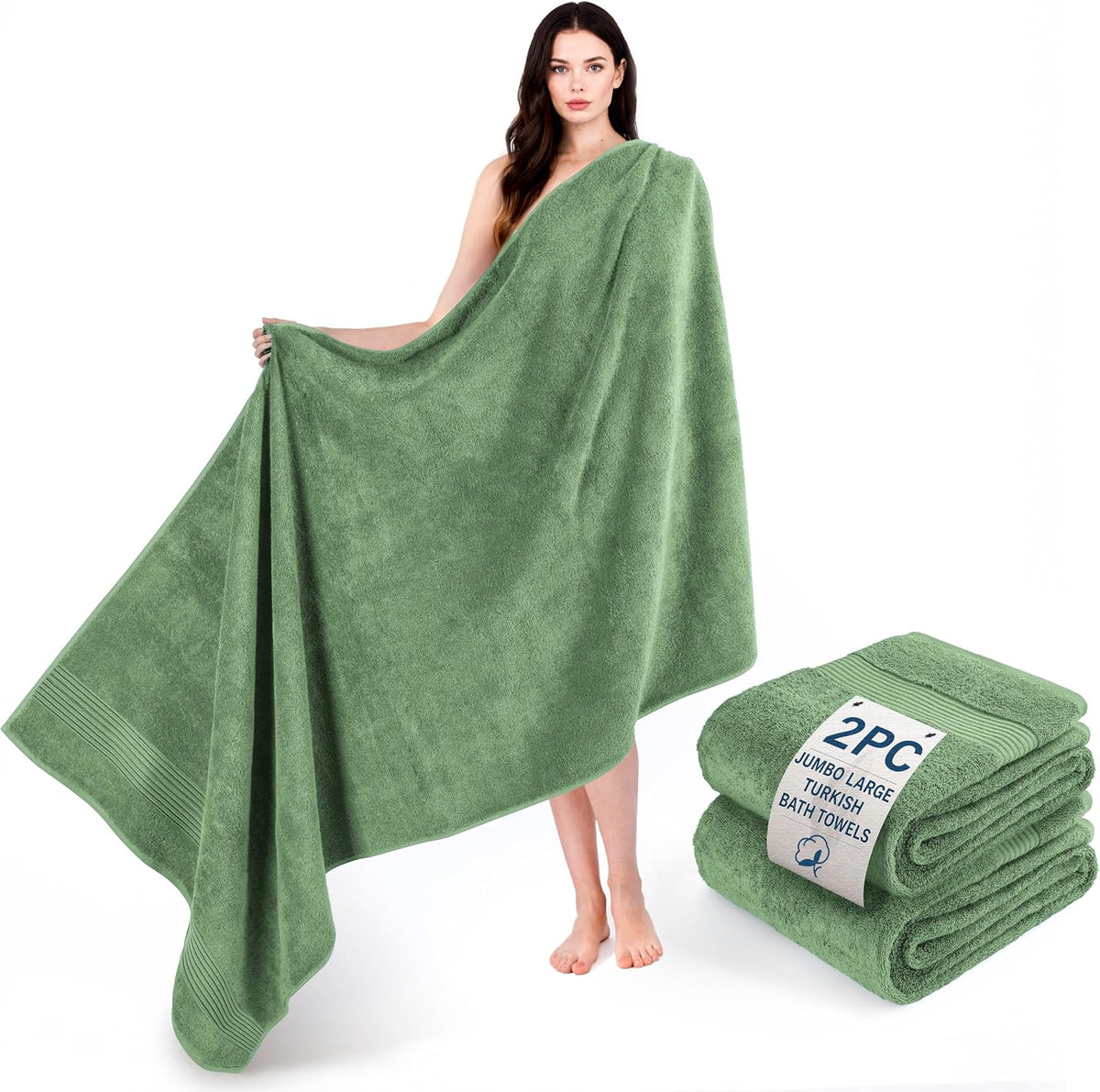 Woman standing barefoot holding a large green bath towel draped across her body with a folded green towel pair beside her