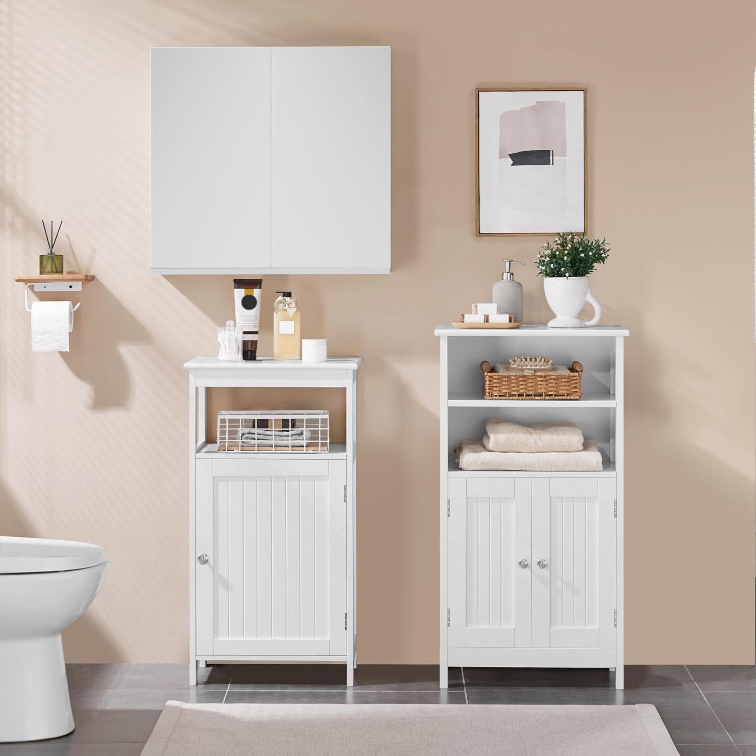 Two white freestanding bathroom cabinets styled in a bathroom scene with towels, decor, and a wall cabinet above