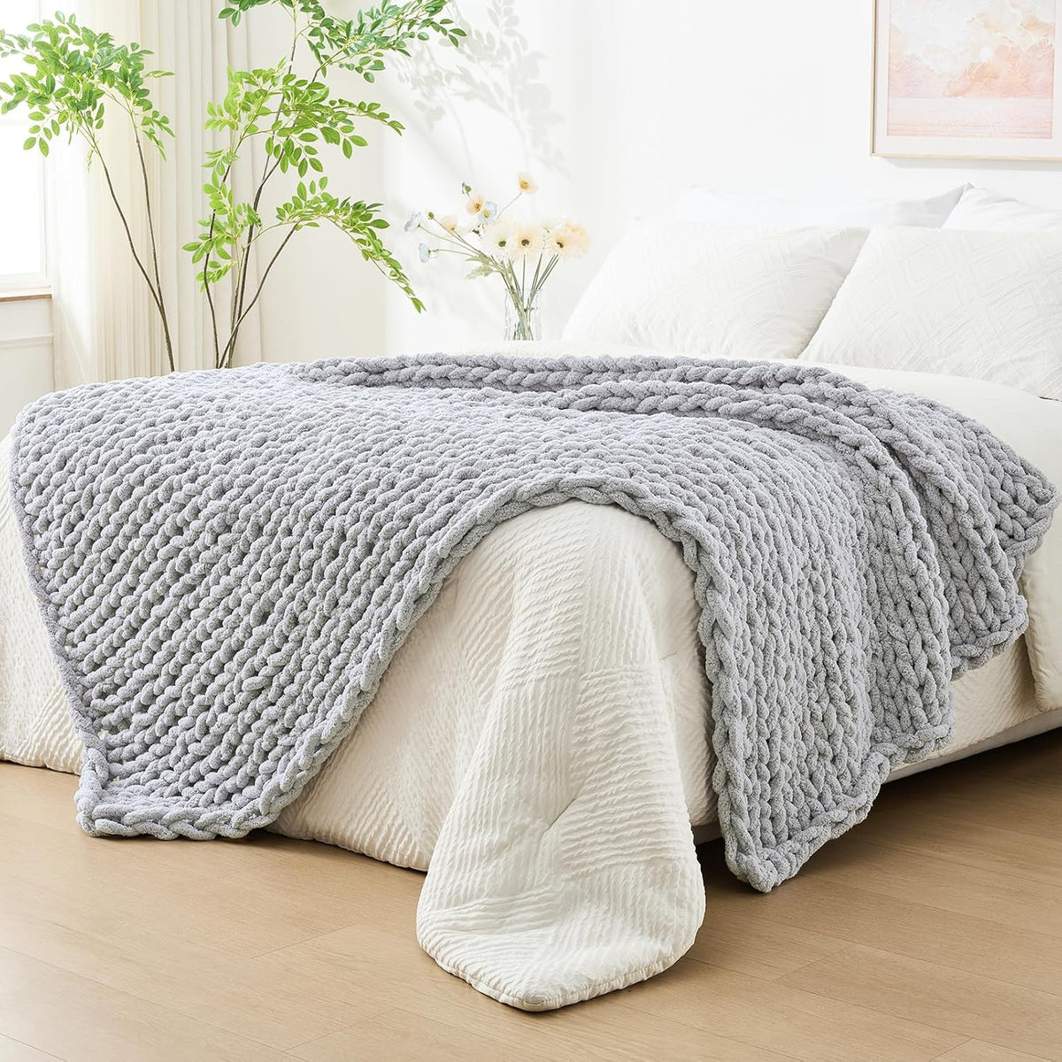 Light-gray chunky knit throw draped across the foot of a bed in a bright bedroom.
