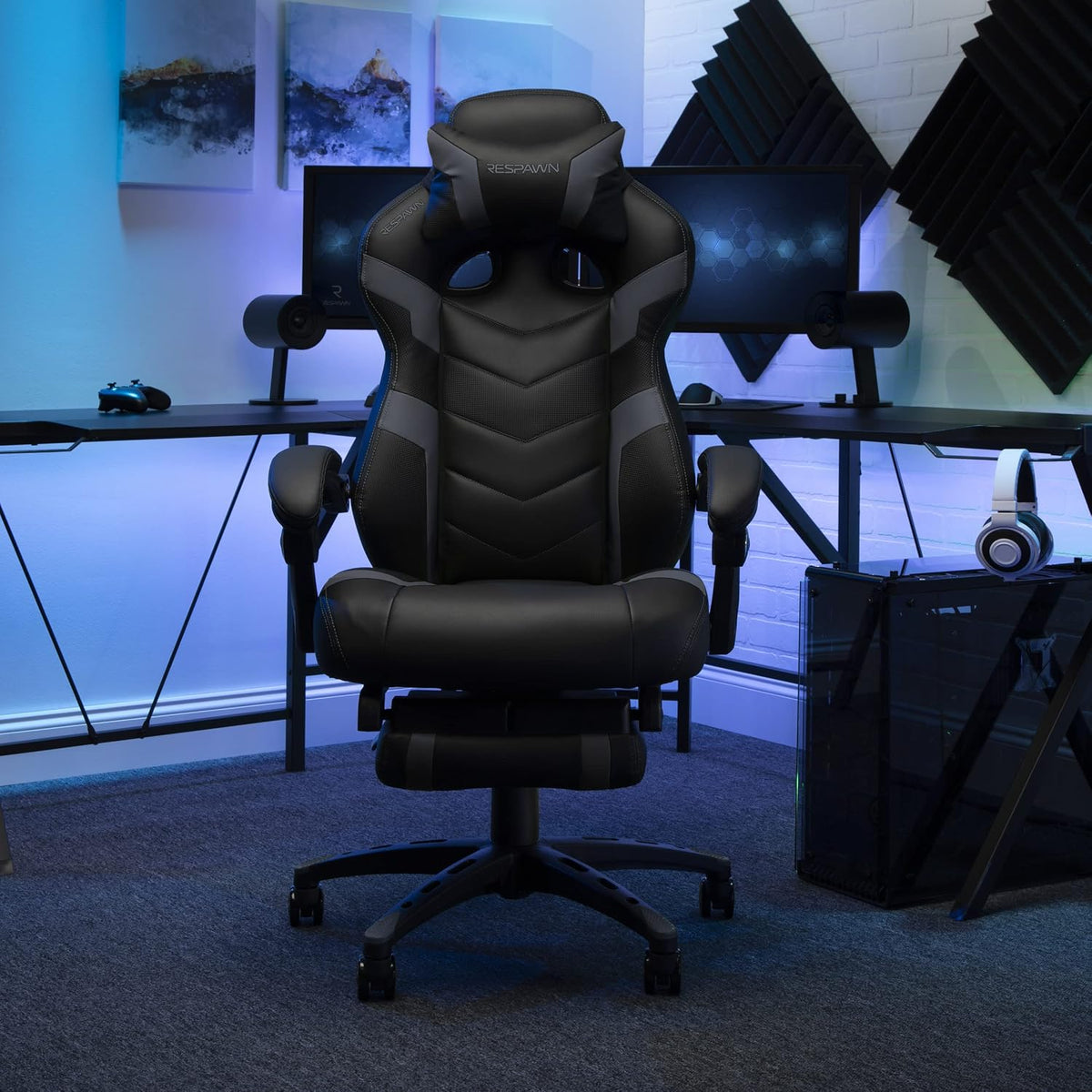 Black and grey gaming chair centered in a dark gaming setup with monitors and blue ambient lighting