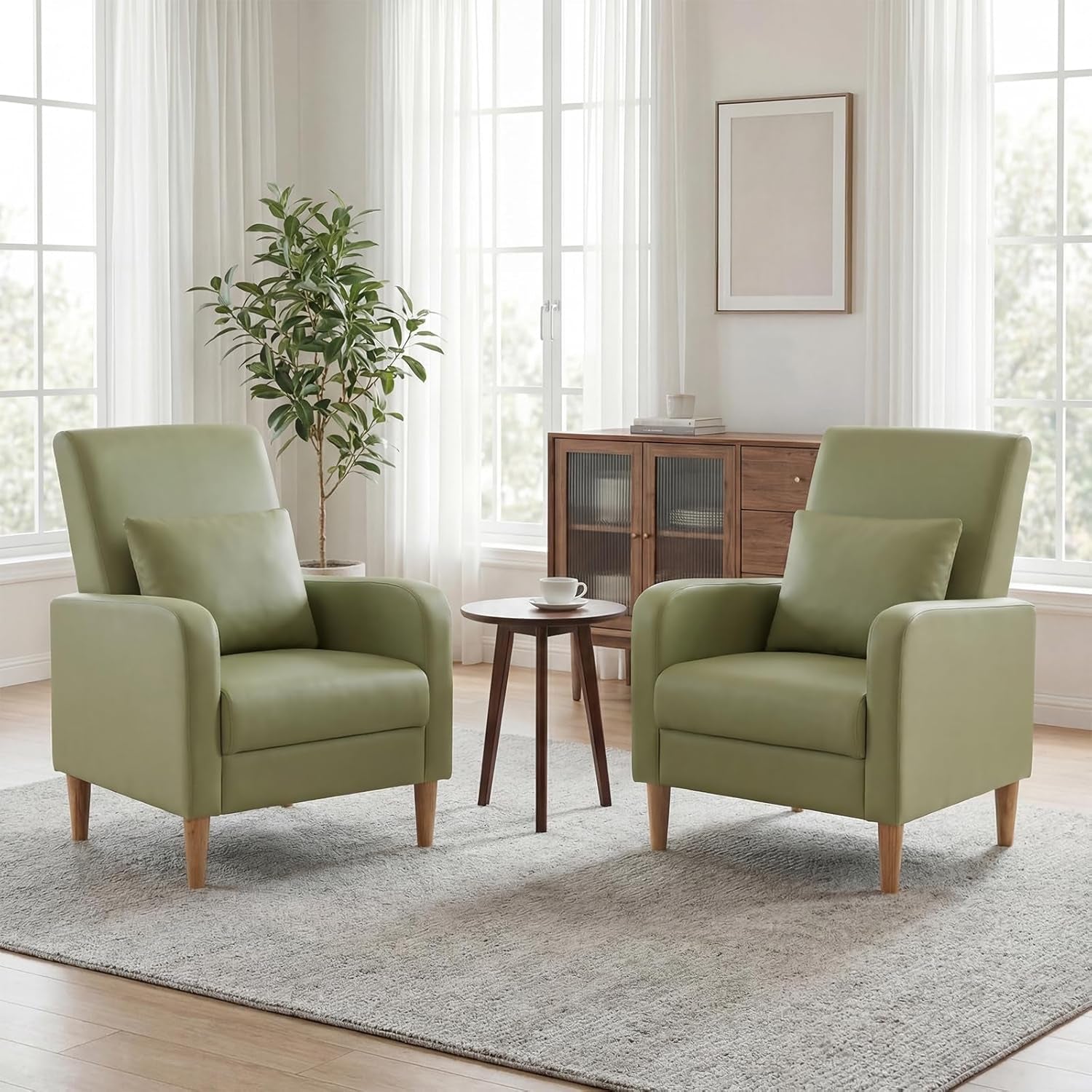 Pair of sage green fabric armchairs with wooden legs arranged around a small round table in a bright room.