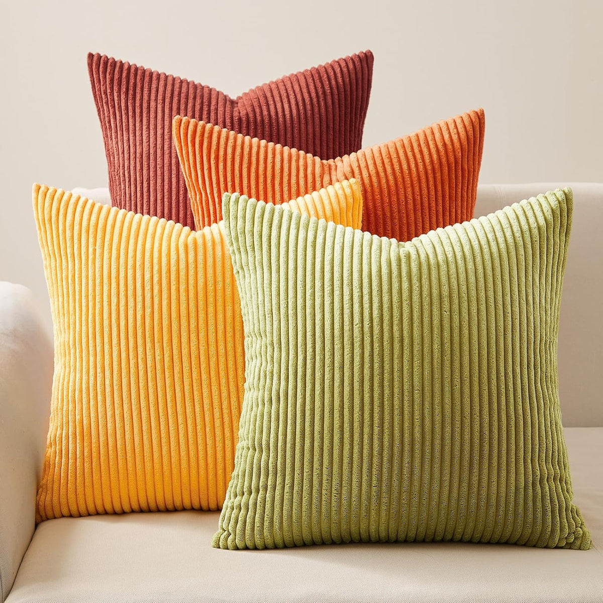 Grouped corduroy cushion covers in green, yellow, orange and rust shown close-up on a cream sofa back