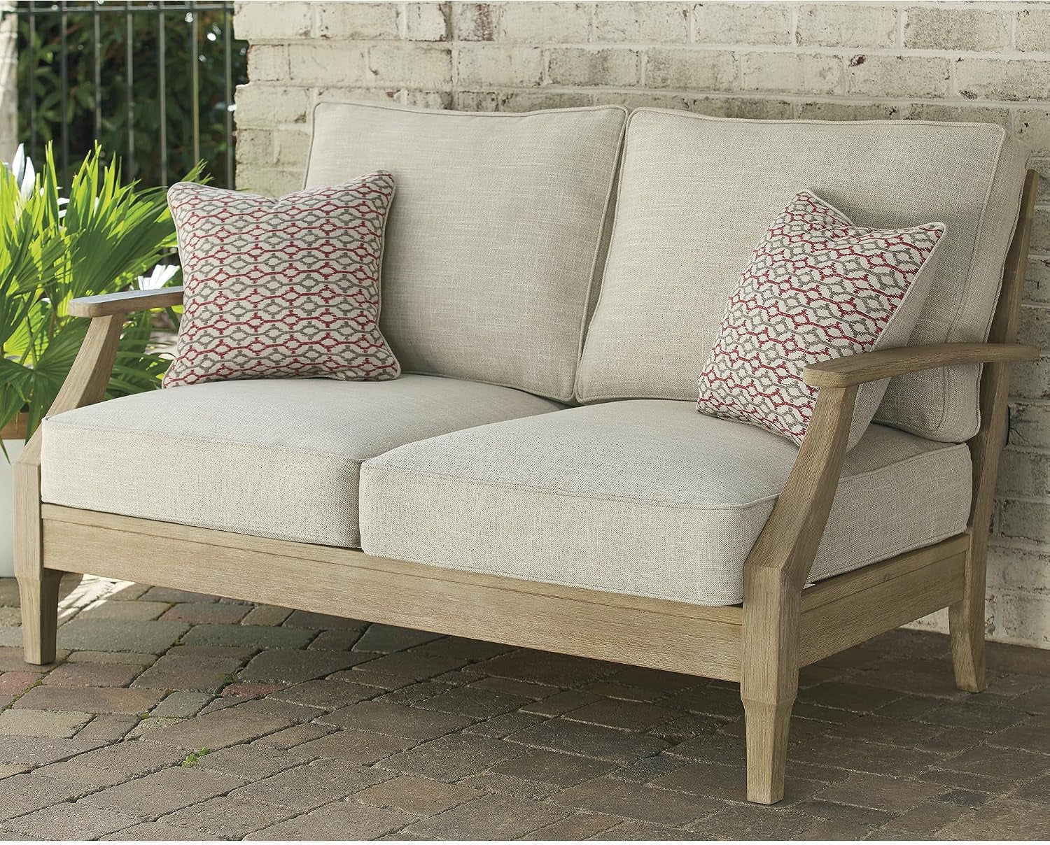 Two-seat view of a beige cushioned eucalyptus frame sofa outdoors against a white brick wall