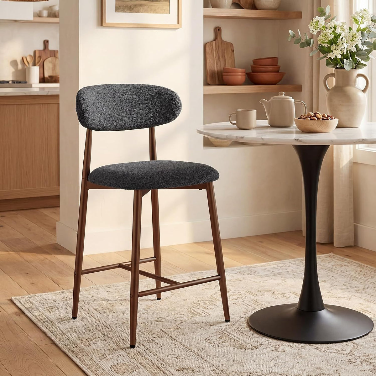 Single dark gray bouclé counter stool next to a small round pedestal table on a patterned rug in a cozy nook
