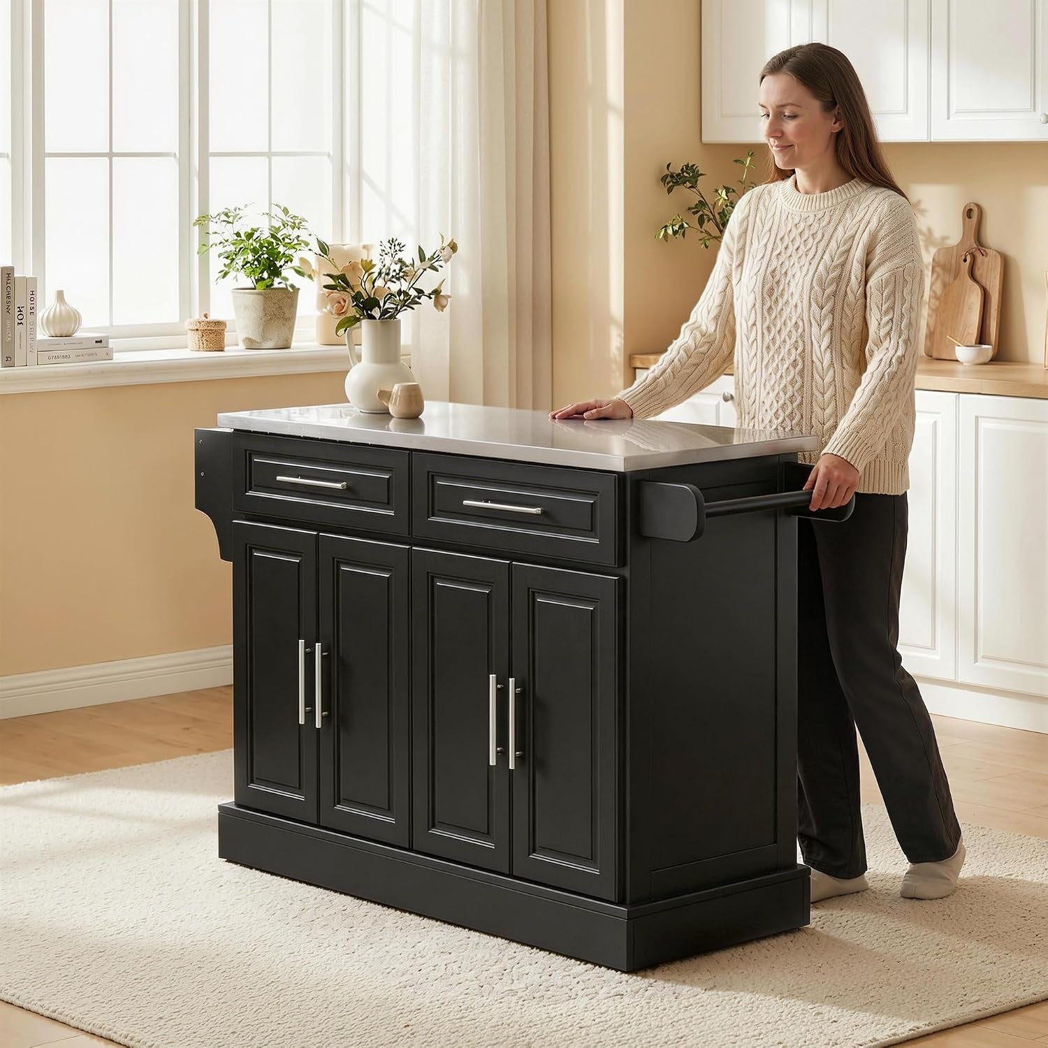 Woman standing by the black island with stainless top in a bright kitchen, holding the side handle.