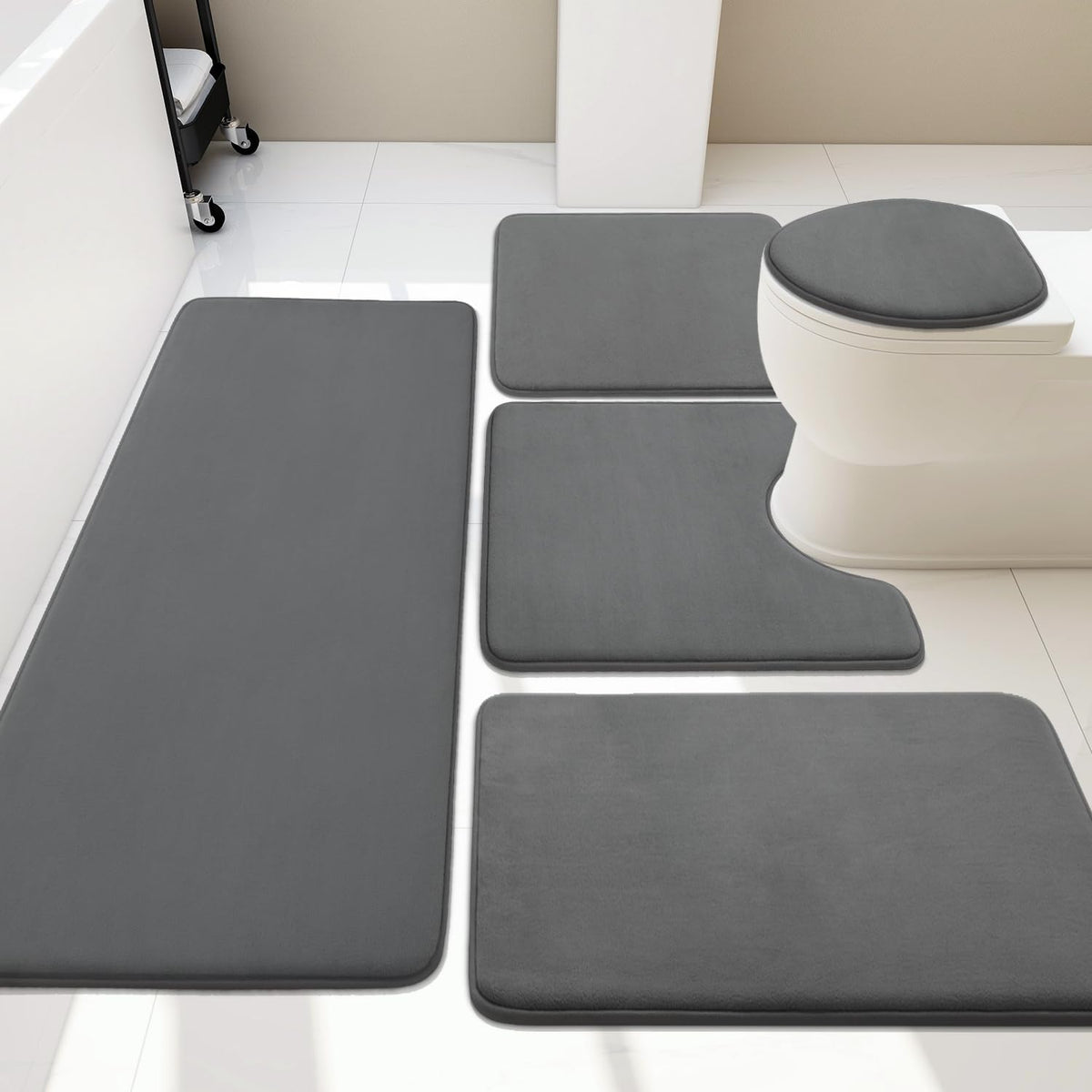 Top-down layout of matching dark gray bath rugs and a toilet seat cover arranged on white tile.