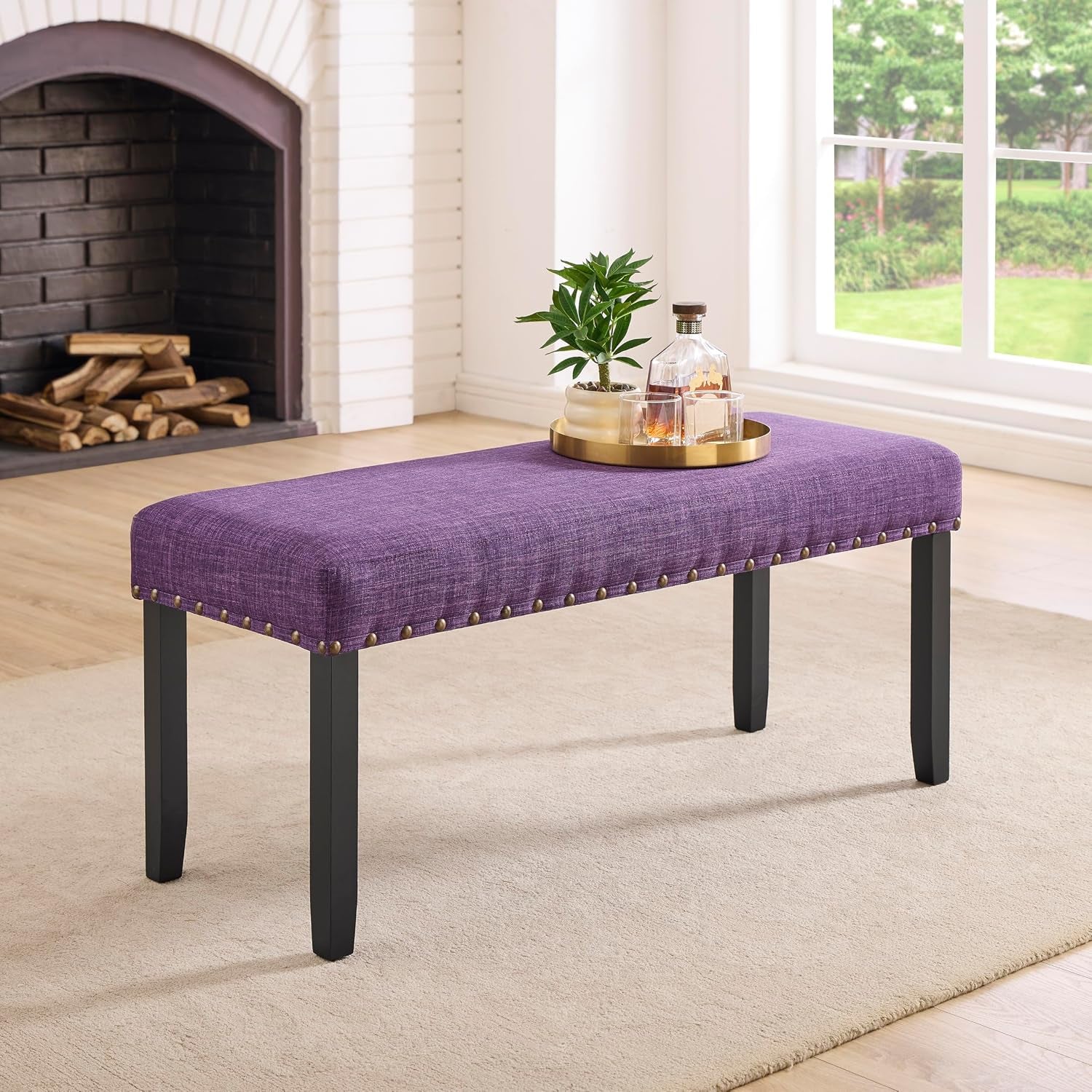 Full view of purple upholstered bench with nailhead trim in a bright living room setting
