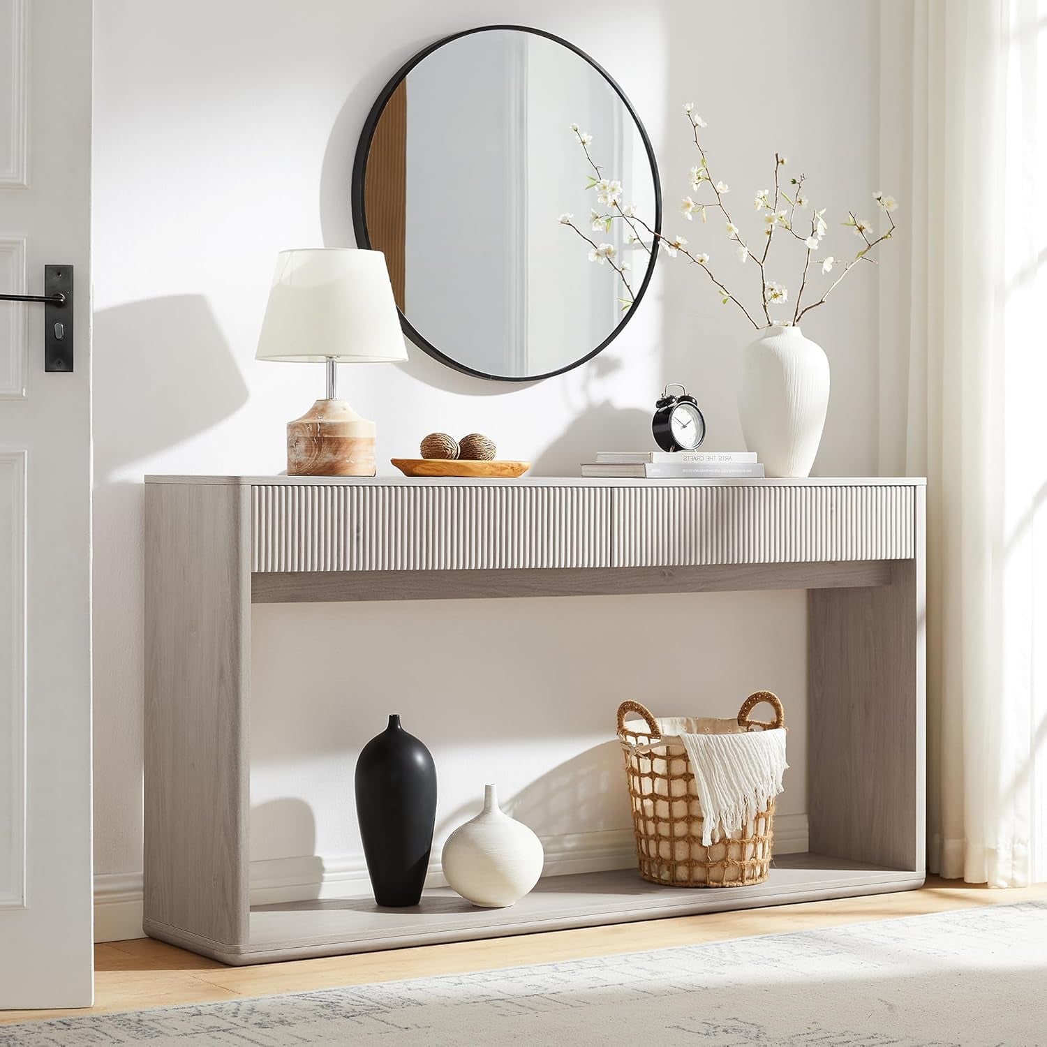 Light gray console table styled under a round mirror with vases and basket on the bottom shelf