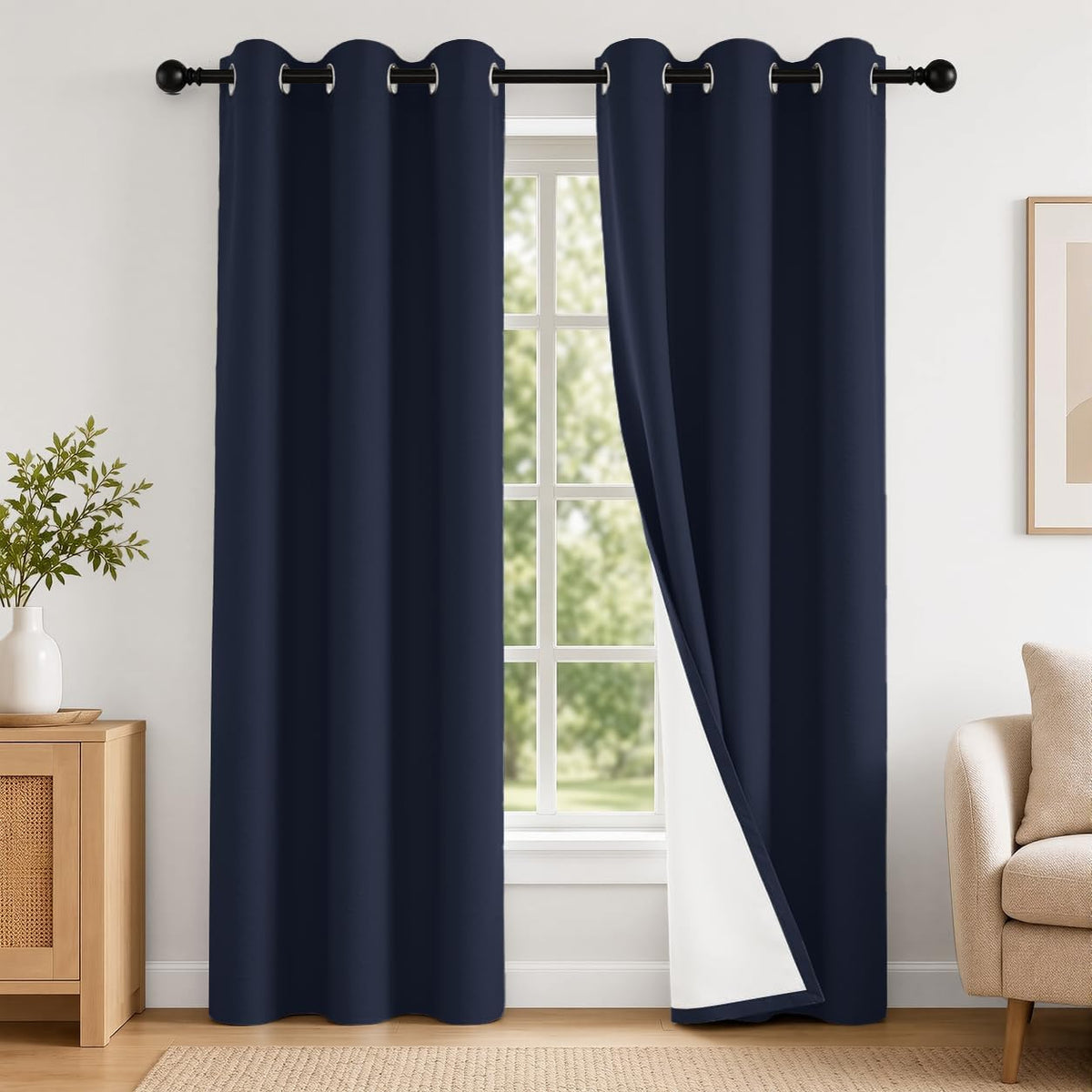 Front view of dark blue grommet curtains on a black rod, one panel folded back revealing white lining, console and armchair