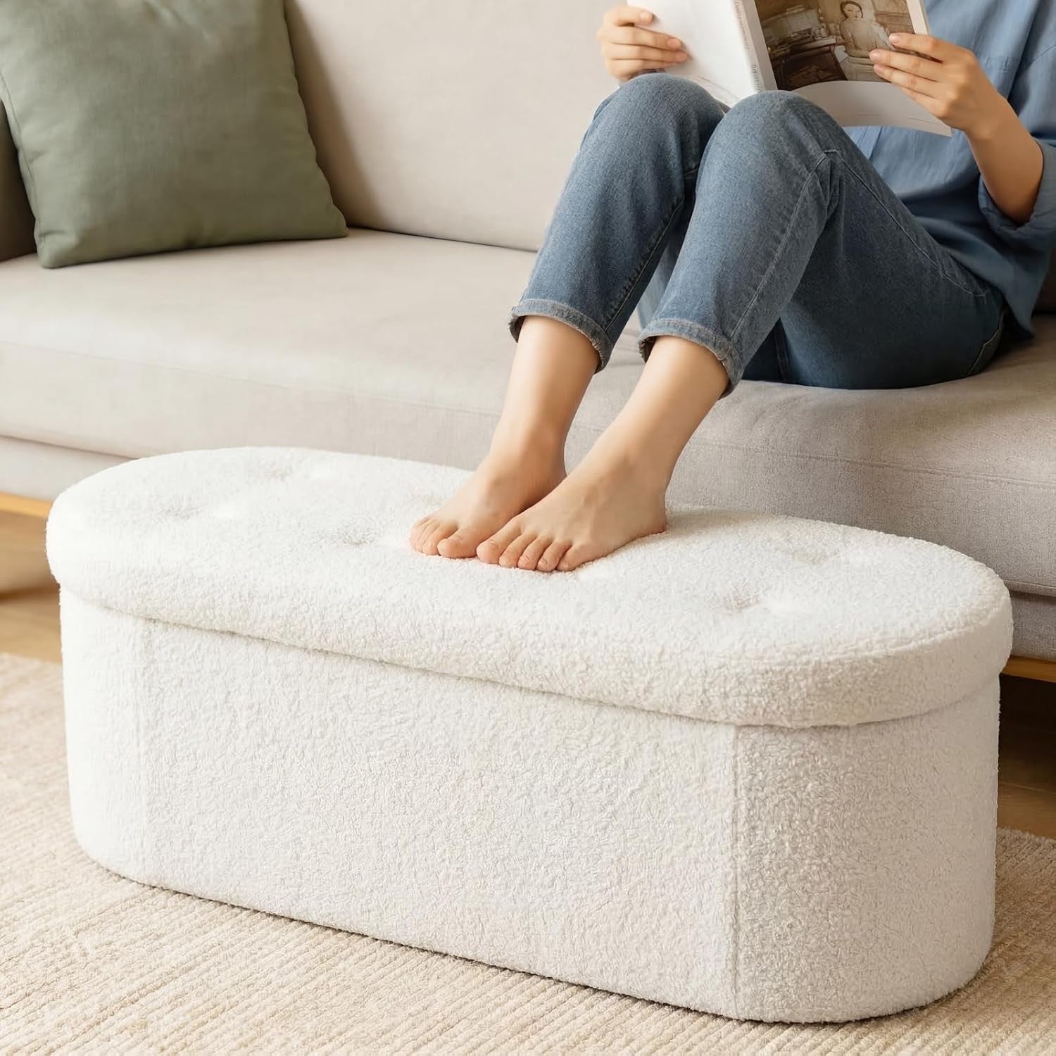 Close front view of white oval ottoman with feet resting on the cushioned tufted top