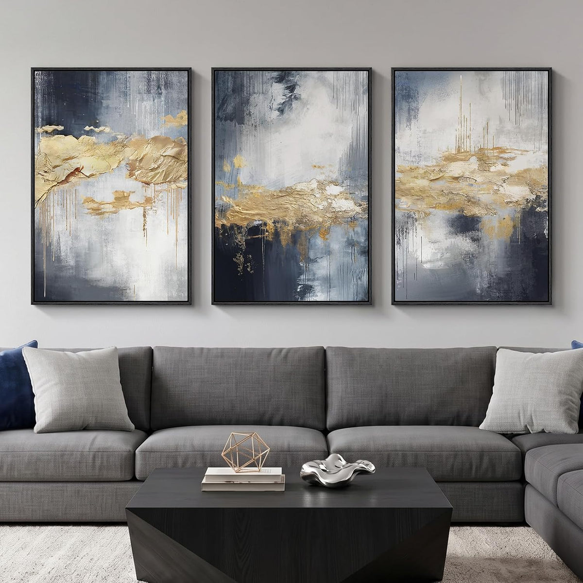 Three vertical abstract paintings in navy, gray, and gold with textured gold accents displayed over a dark gray couch.