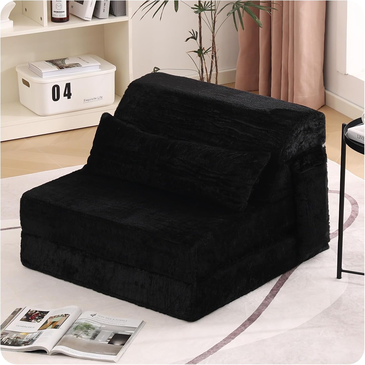 Black folding sofa bed set up as a chair on a rug beside a plant and open magazine
