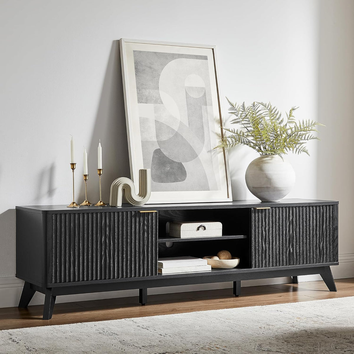Low dark wood TV stand with fluted sliding doors, open center shelves, decor and framed art on top