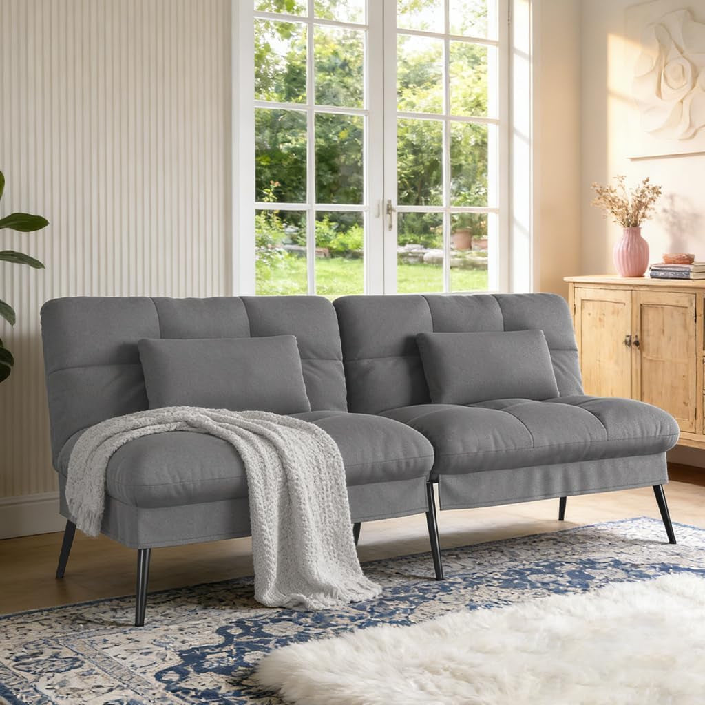 Charcoal gray fabric futon sofa with lumbar pillows and a casually draped blanket near a wood cabinet.