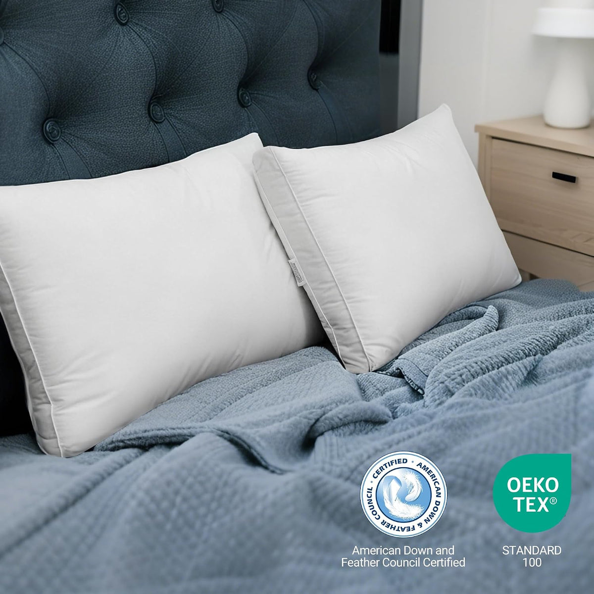 Two white pillows propped against a dark tufted headboard on a bed with a textured blue blanket