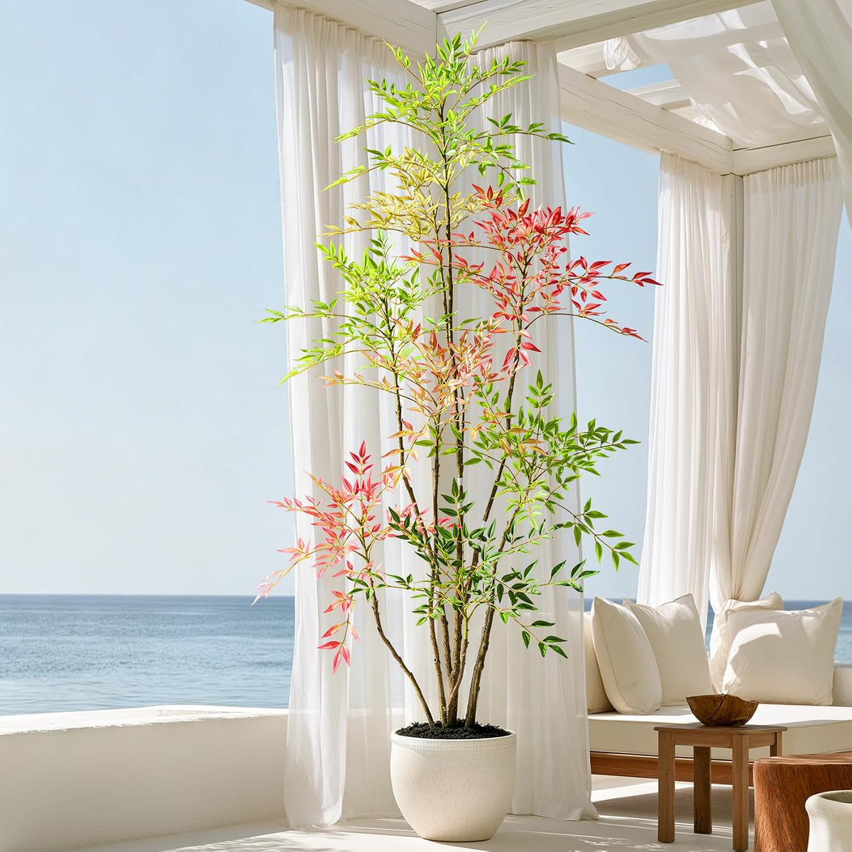 Faux nandina staged under a breezy white cabana with sheer curtains, ocean visible in the background and lounge seating to