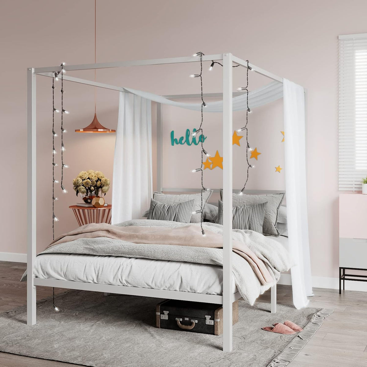 Main room shot of a white metal canopy bed with sheer drapes, string lights, layered bedding and a suitcase under the frame.