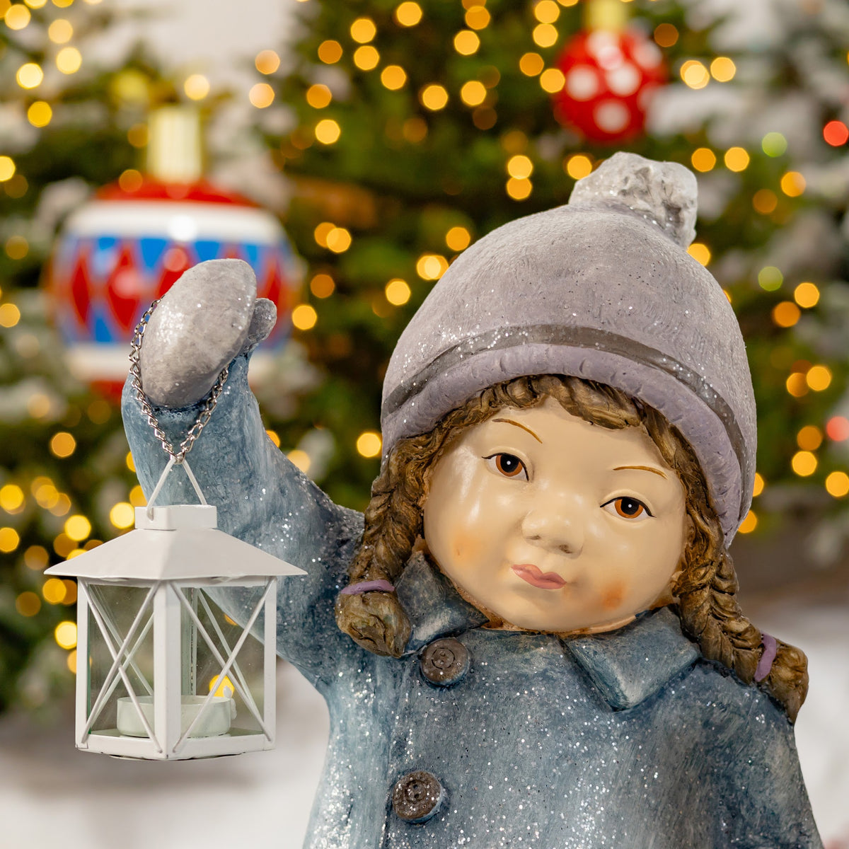 Close-up of a child figure in a gray knit hat holding a white lantern.