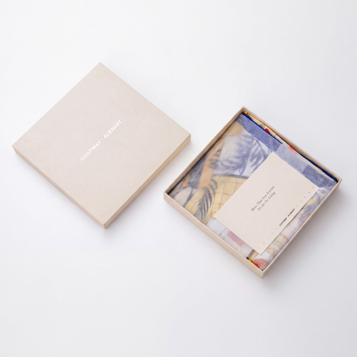 Open beige gift box holding a folded patterned scarf and a card, with the lid beside it.
