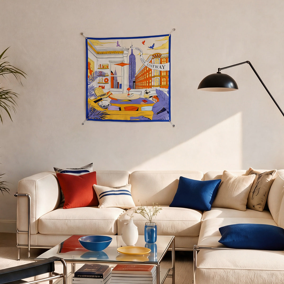 Blue-bordered illustrated scarf displayed above a cream sofa in a sunlit living room.