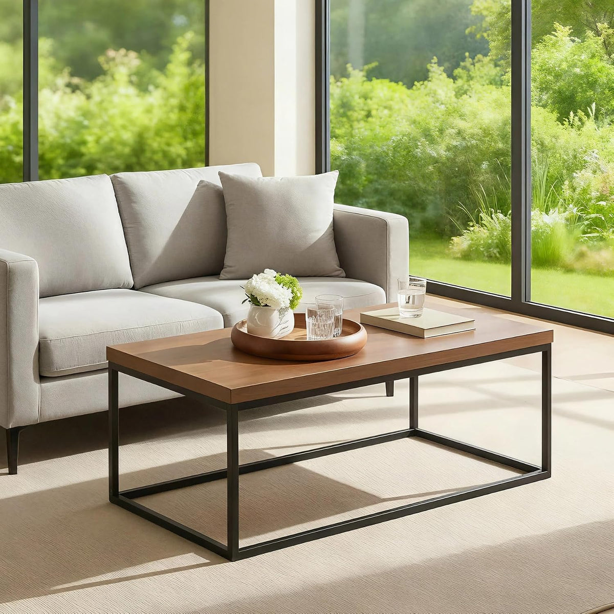 Medium-tone wood rectangular coffee table with matte black rectangular metal base in a sunlit seating area with a sofa.