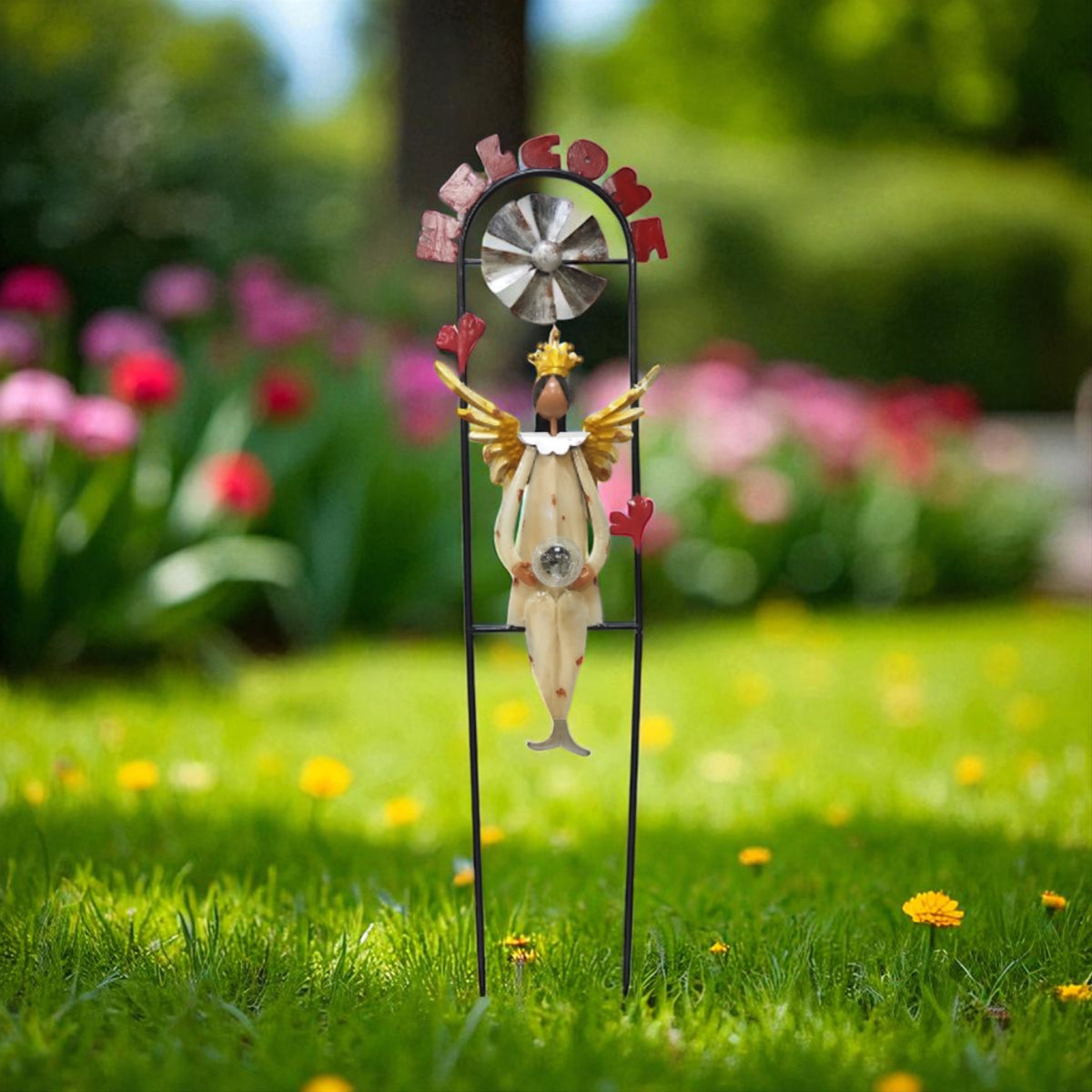 Front view of a winged angel beneath a small metal windmill, framed by a tall garden stake.