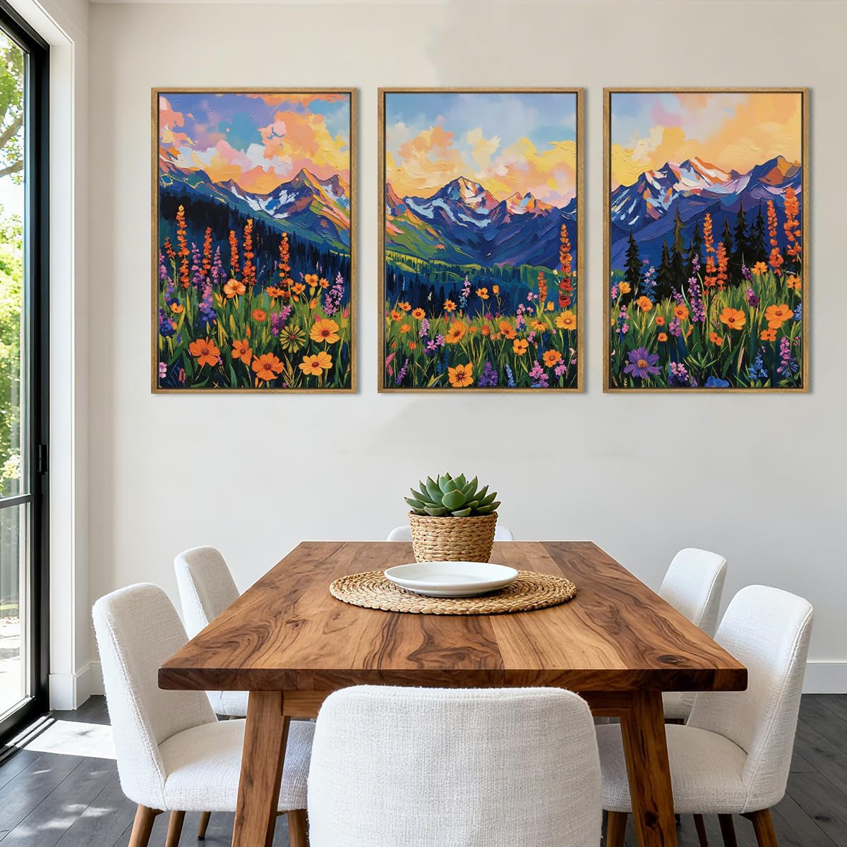 Dining area with wooden table and three colorful mountain and wildflower paintings in frames above.