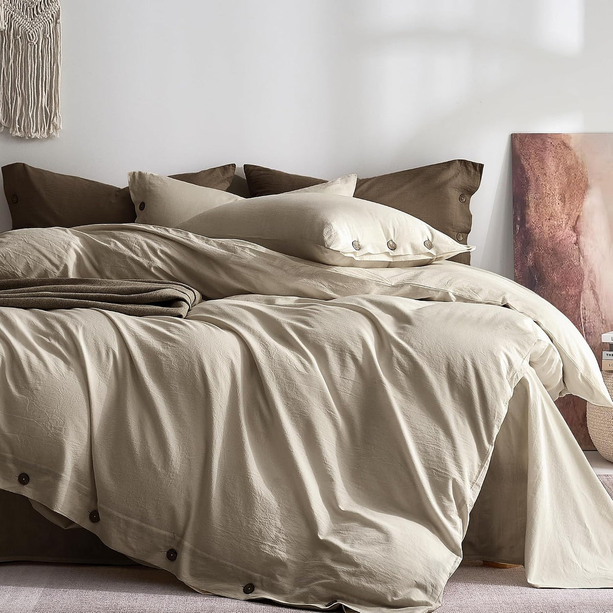 Close-up main view of an unmade bed with cream duvet, brown back pillows and button details on the hem.