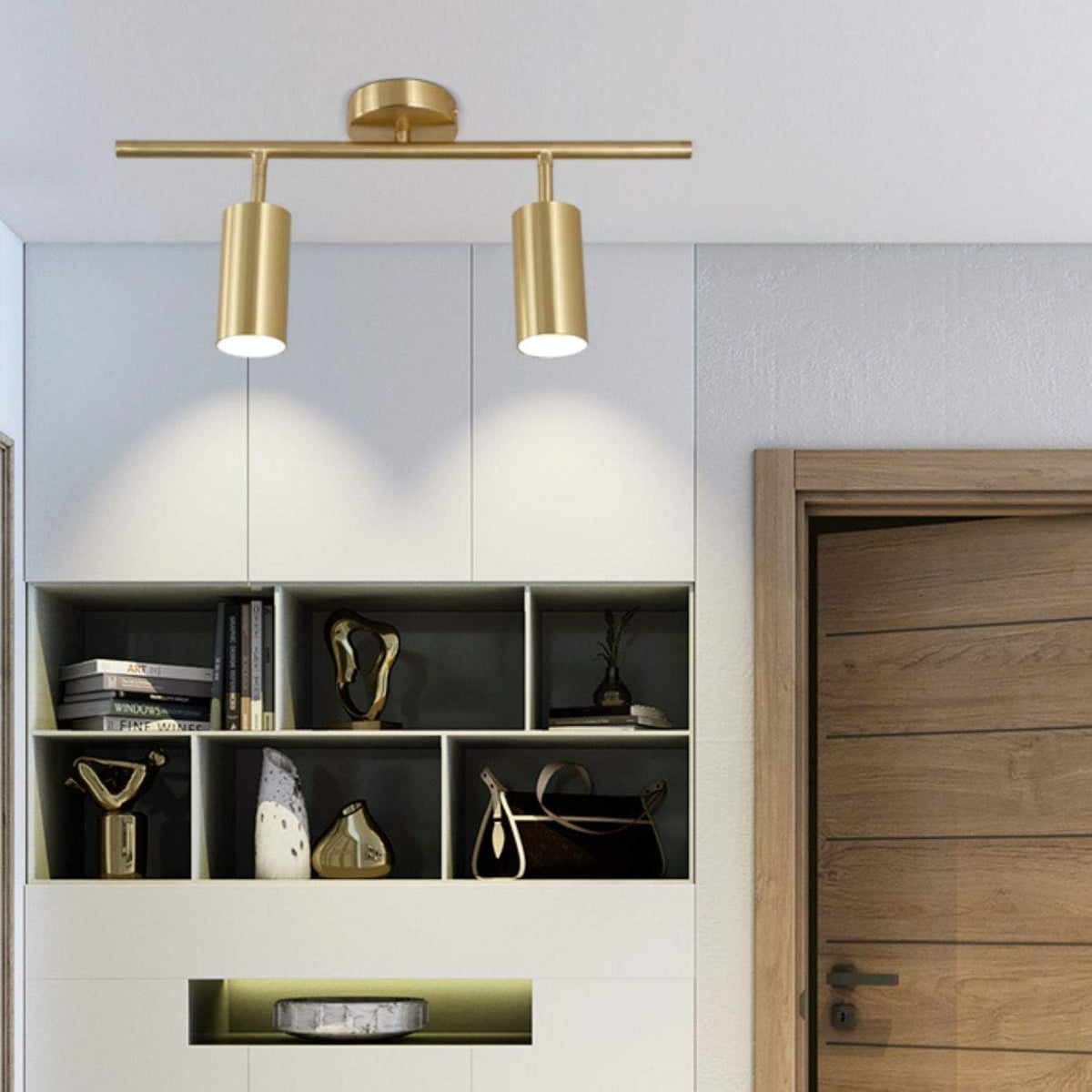 Gold two-head track light installed on a white ceiling above shelving with light illuminating the wall below