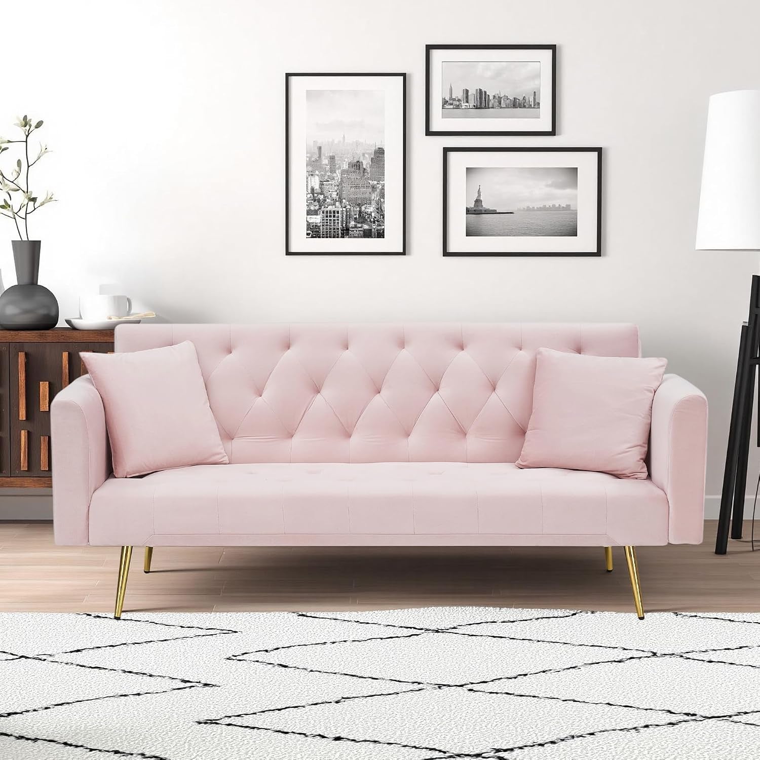 Blush pink velvet tufted sofa with gold tapered legs and two matching pillows in a living room.