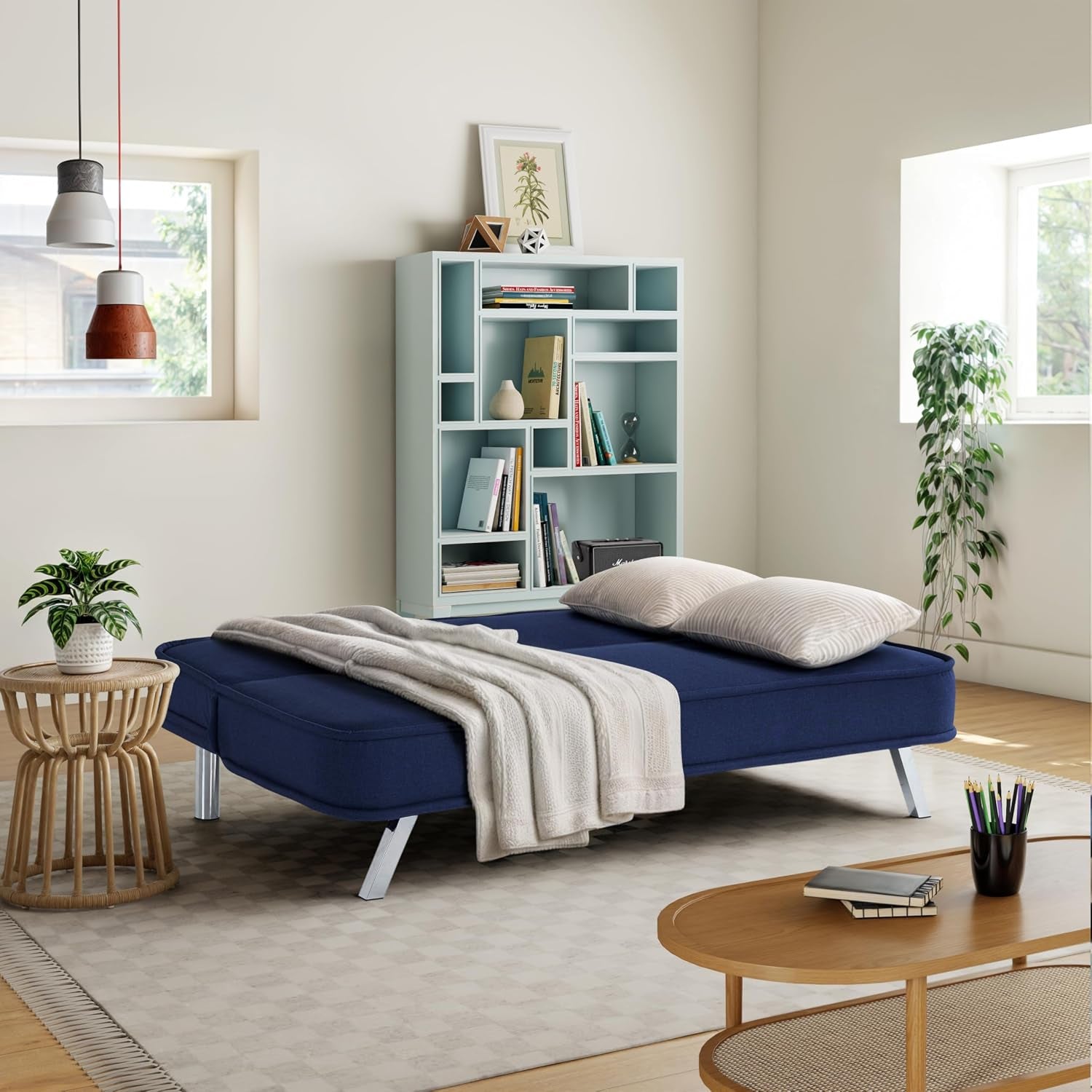 Navy futon sofa converted to a flat sleeper in a living room setting with blanket and pillows