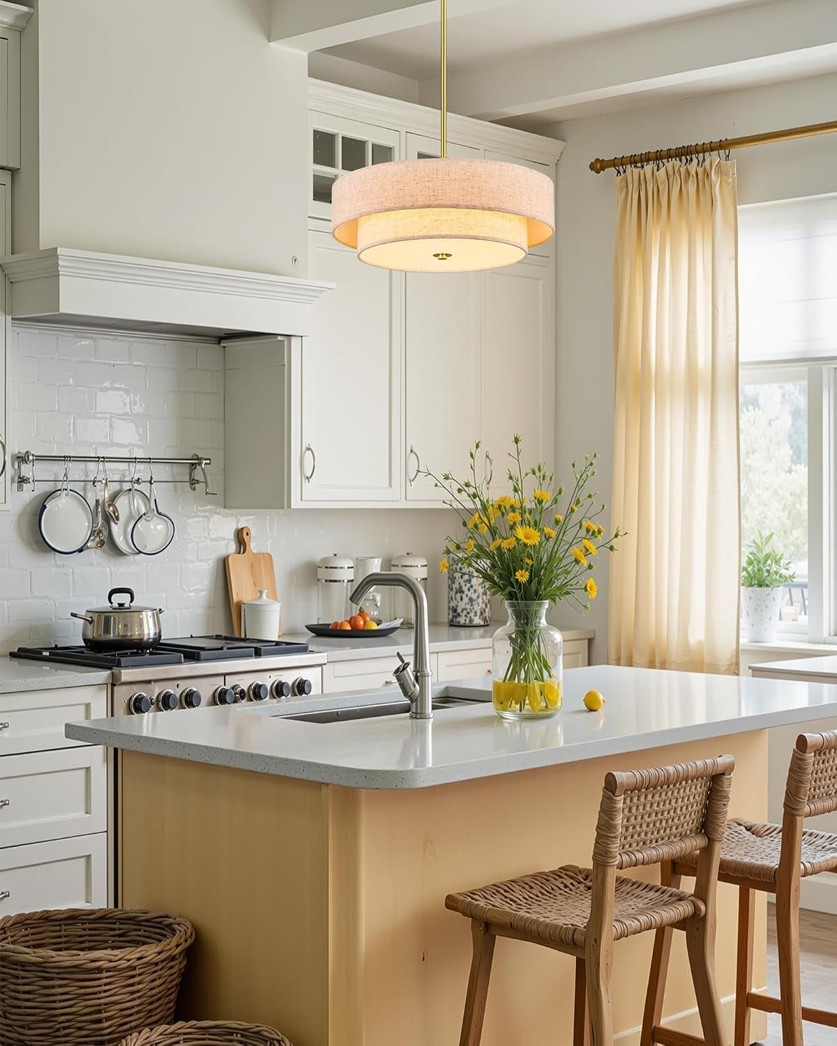 Kitchen island scene with a lit two-tier linen drum chandelier suspended on a brushed gold rod.