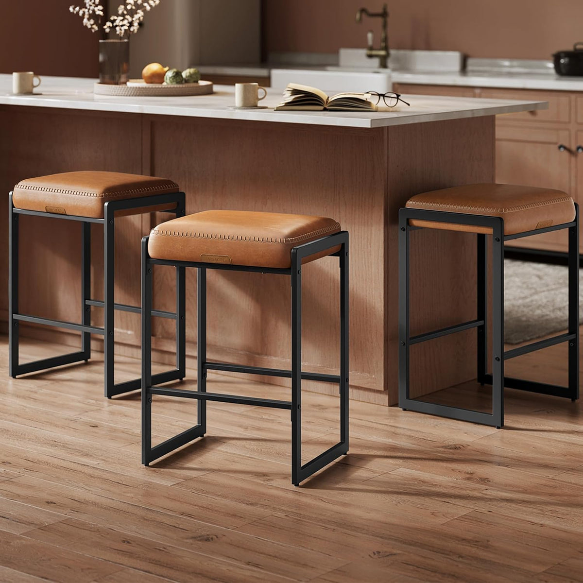 Three caramel-cushioned counter stools with black frames lined along a kitchen island with an open book on the counter.