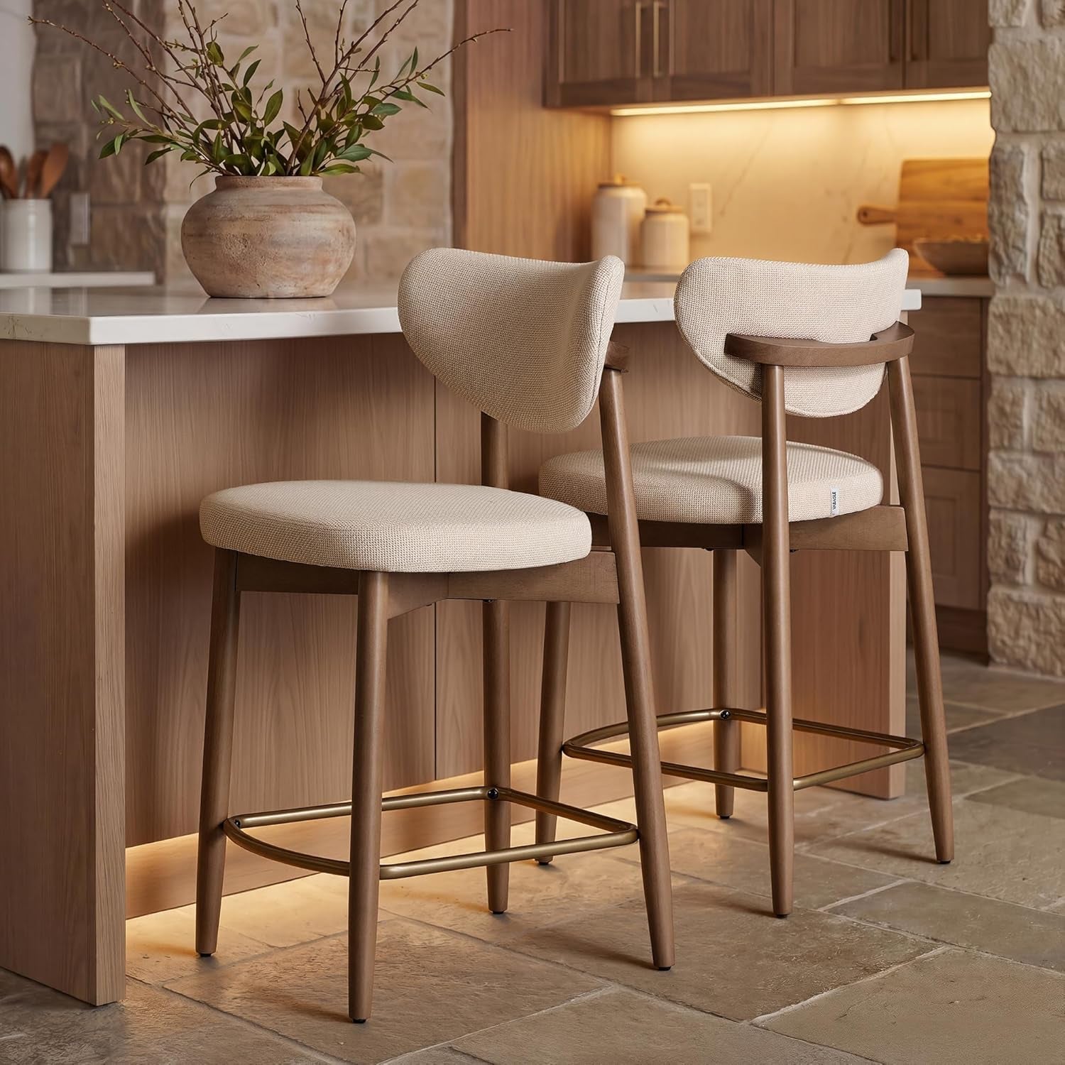 Pair of beige counter stools at a kitchen island, side view showing curved backrests and metal footrests.