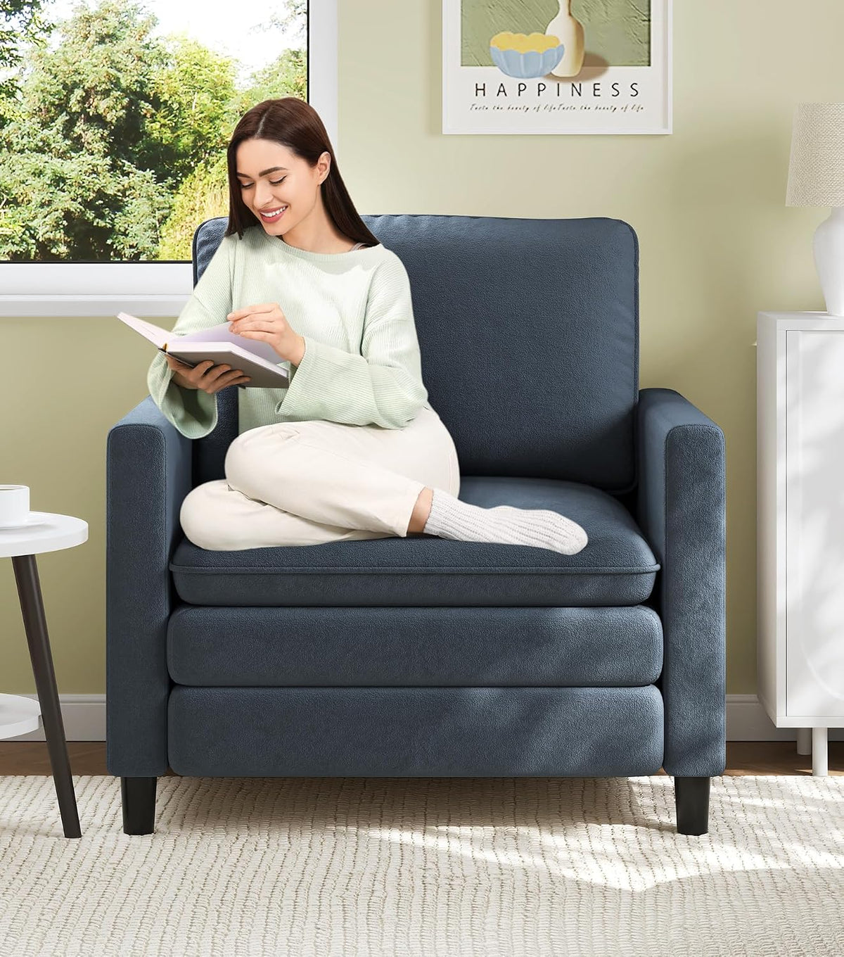 Blue-gray small loveseat with a woman reading while sitting cross-legged