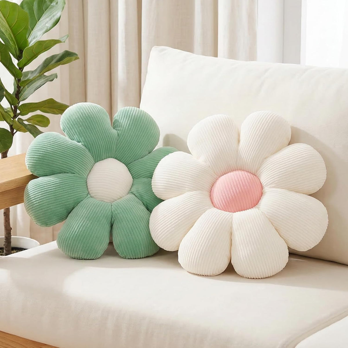 Pair of daisy cushions in mint green and ivory shown on a sofa arm and seat with sheer curtains behind.
