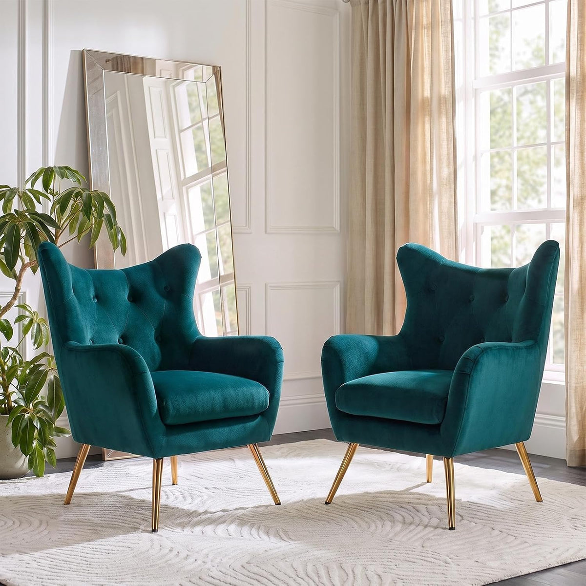 Two deep teal velvet wingback chairs with button tufting and metallic legs beside a leaning mirror.