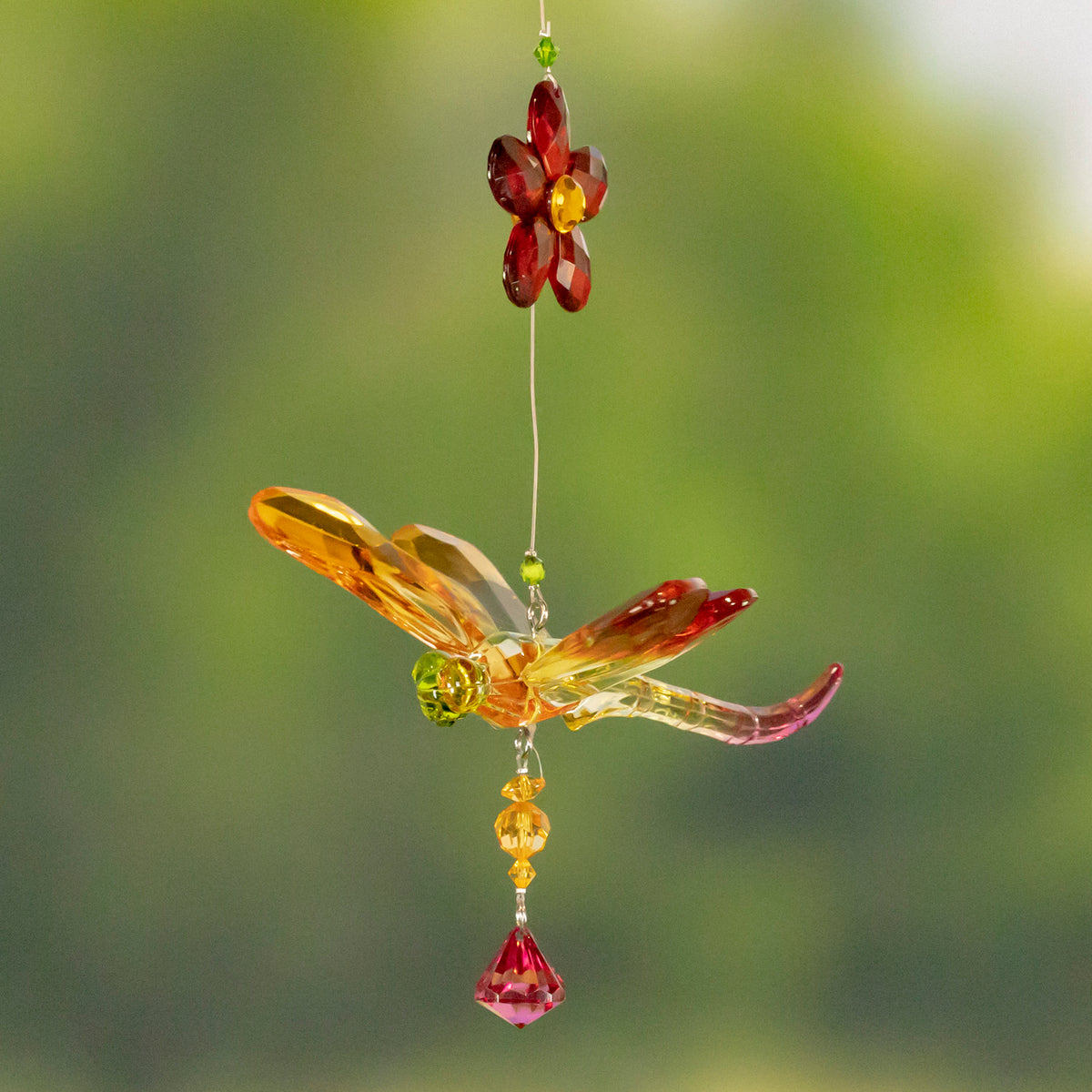 Amber and red faceted dragonfly ornament hanging beneath a red flower, with a dangling pink crystal.