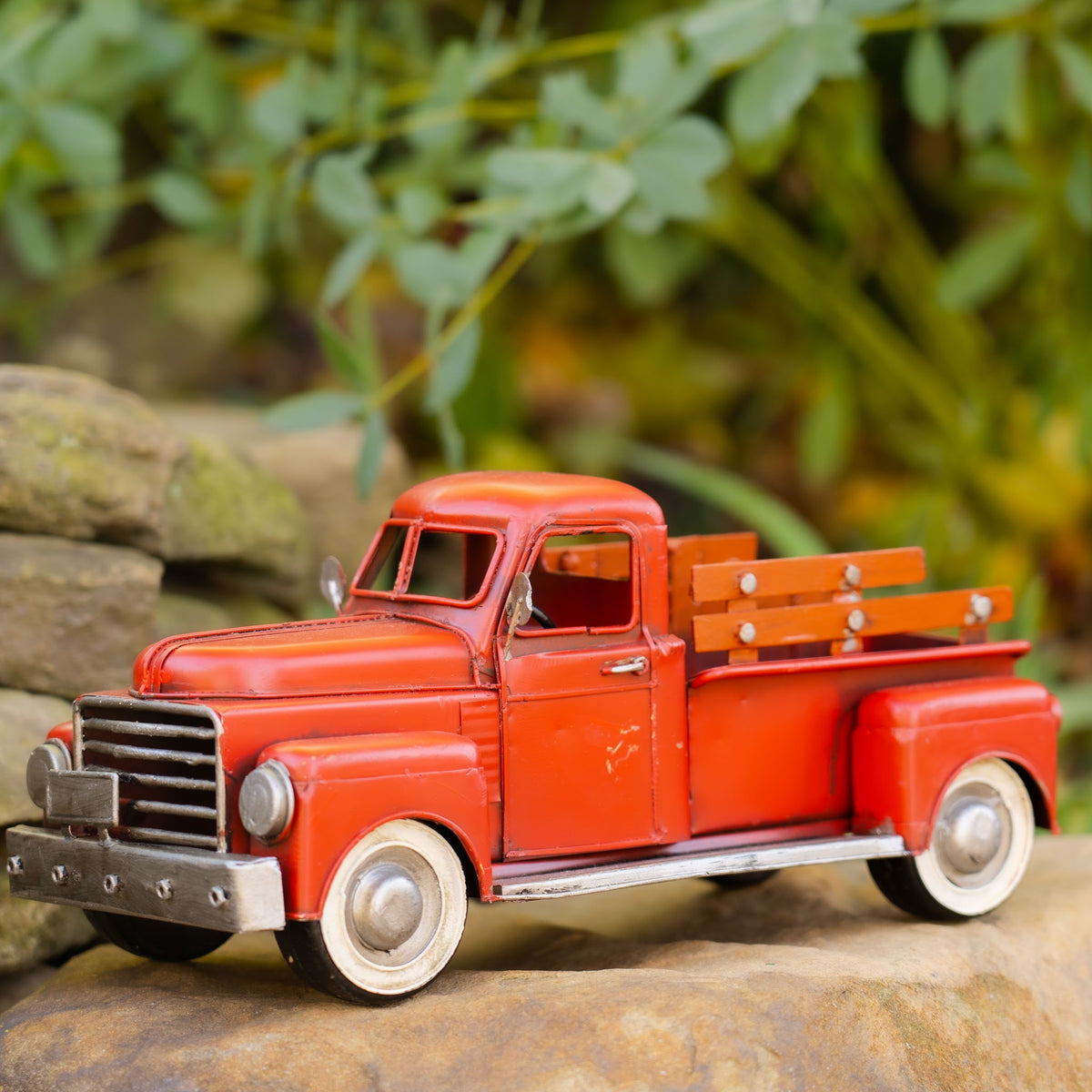 Red vintage-style pickup truck with white-rimmed wheels and wooden-look bed rails, posed on a rock outdoors.