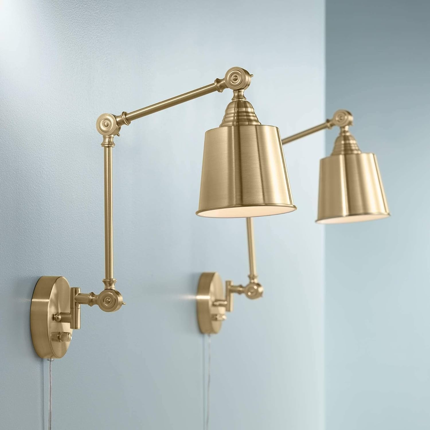 Two antique brass swing-arm wall lamps mounted on a light blue wall, side perspective showing adjustable arms