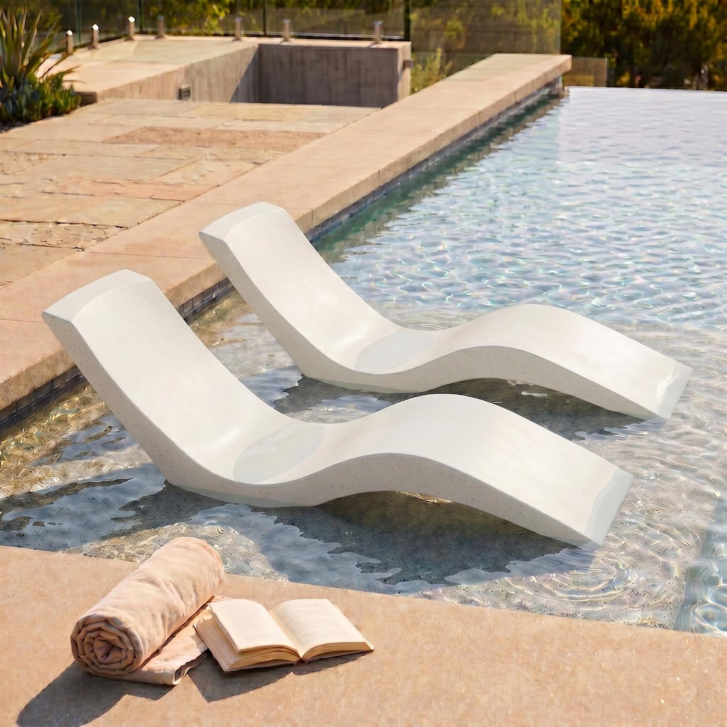 Two white contoured resin loungers placed on a sun shelf in shallow pool water with a rolled towel and open book on the deck