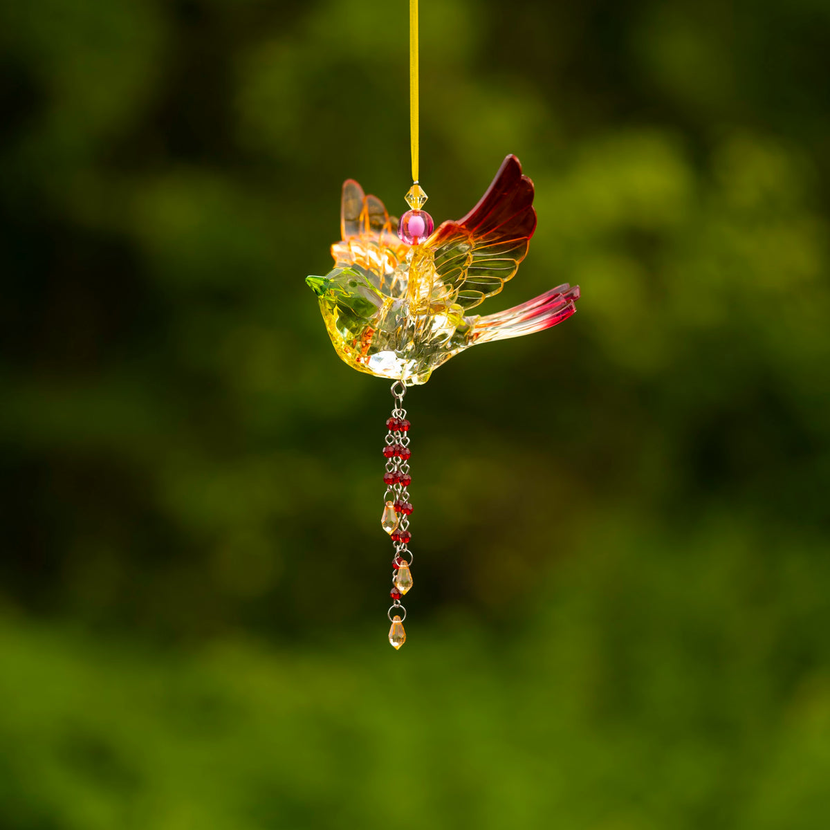 Side view of a translucent bird ornament with a raised dark red wing and a long jeweled tail.