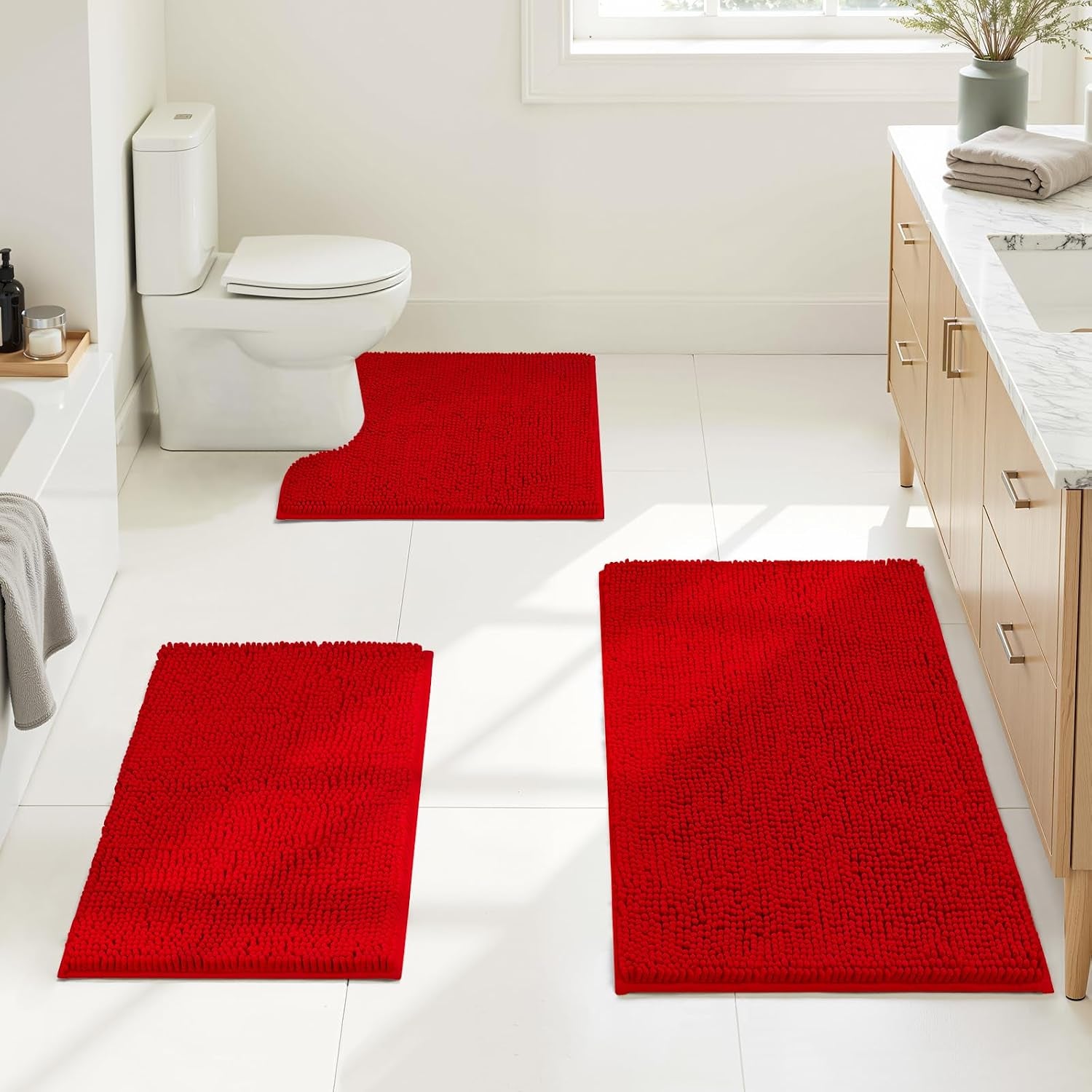 Bright red chenille bath rug set arranged on a white bathroom floor near a vanity, bathtub, and toilet