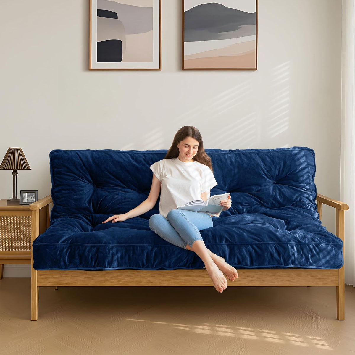 Blue futon mattress on a light wood sofa frame with a person sitting and reading in natural light.