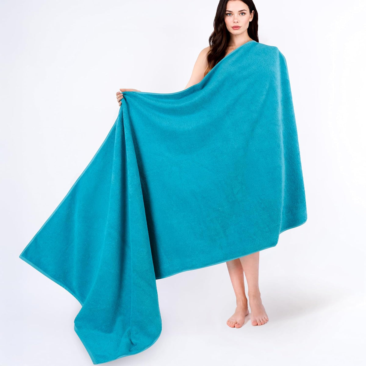 Woman holding and draping a large teal bath towel, standing against a white background