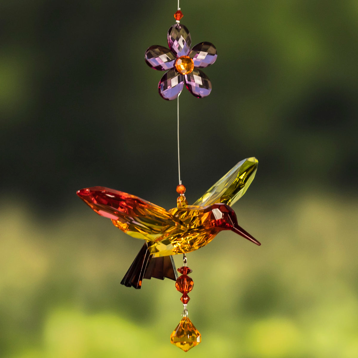 An amber and red faceted hummingbird hangs beneath a purple flower and above a matching bead.