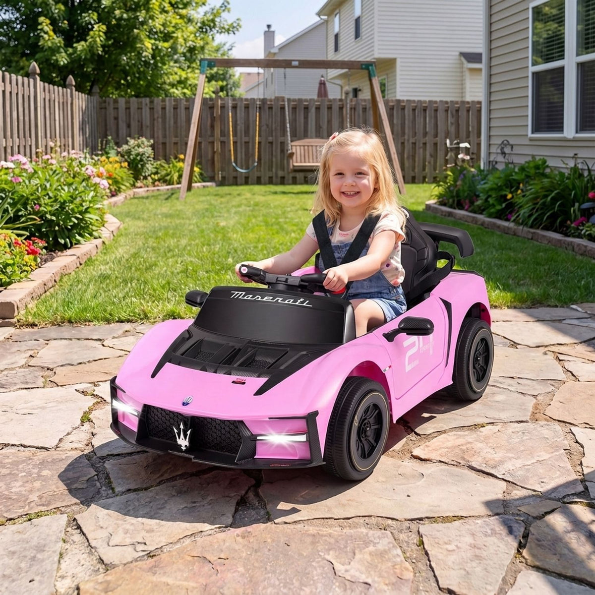 A smiling child sits in a pink ride-on car on a stone patio.