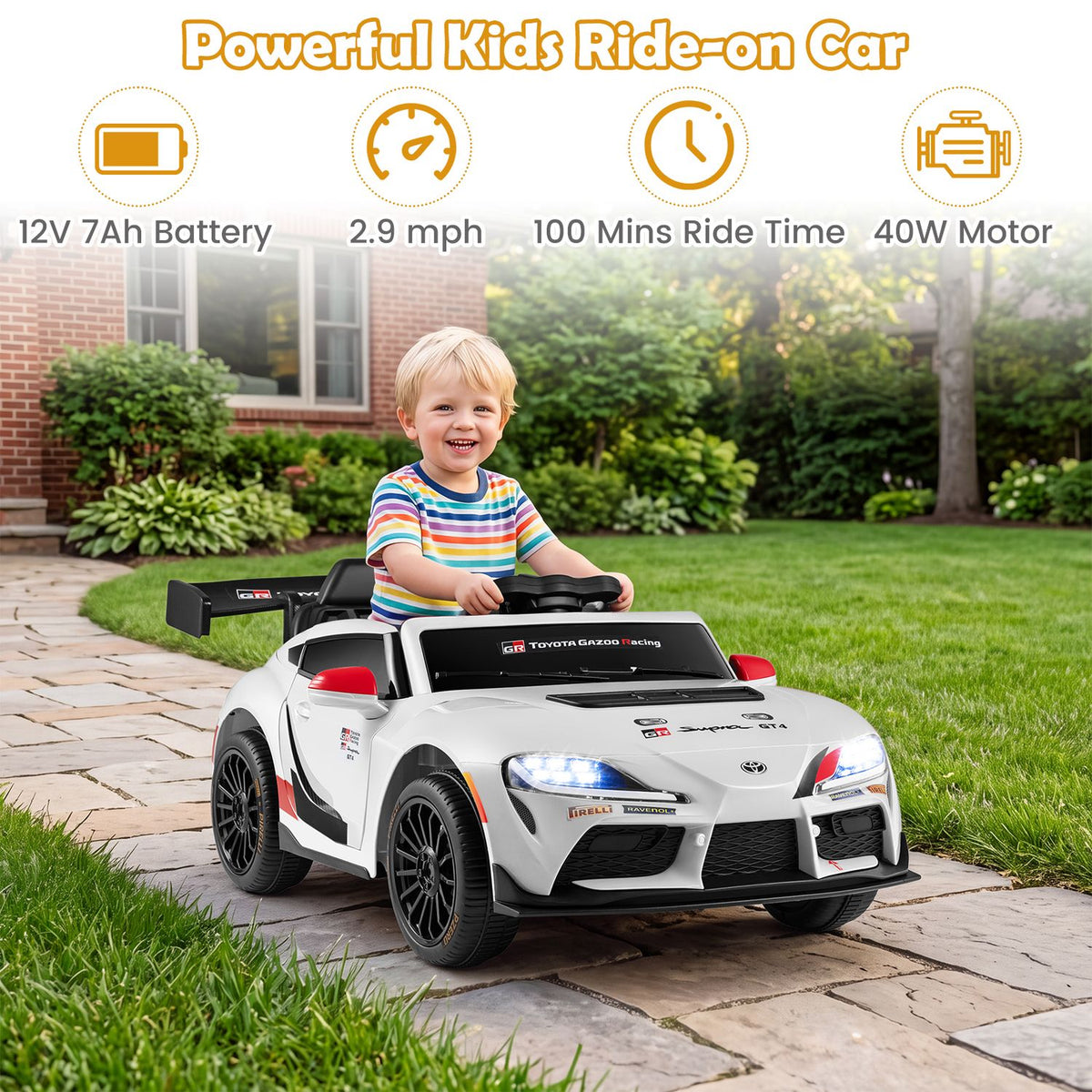 A child sits in a white ride-on car on a garden path, with its headlights on.