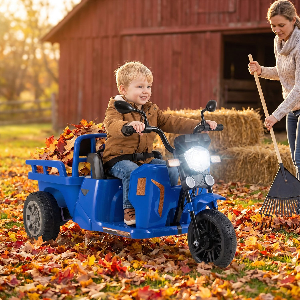 A child rides a blue three-wheeled vehicle with a trailer through fallen leaves as an adult rakes nearby.