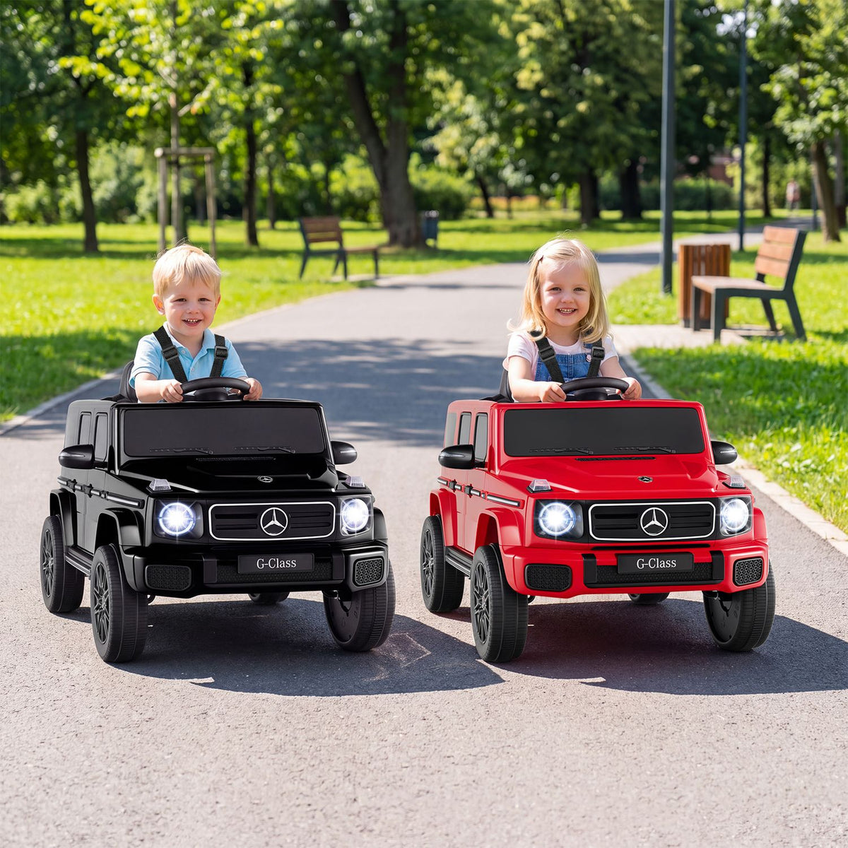 Two children sit in black and red miniature SUVs on a park path.